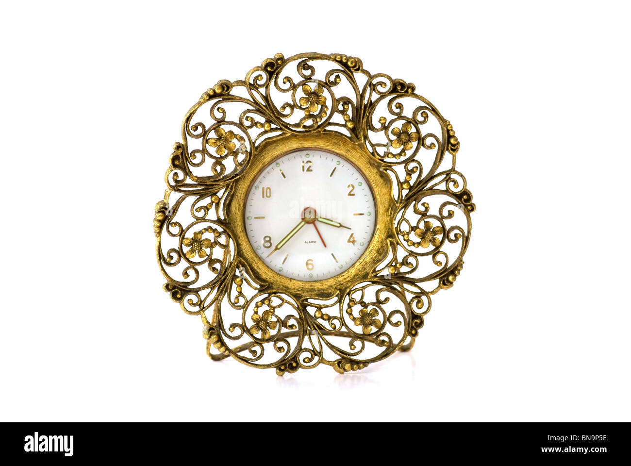 Ornate vintage fifties gold metal alarm clock with stand - isolated. The fancy clock is surrounded by metal twisted into curls like lace. Stock Photo