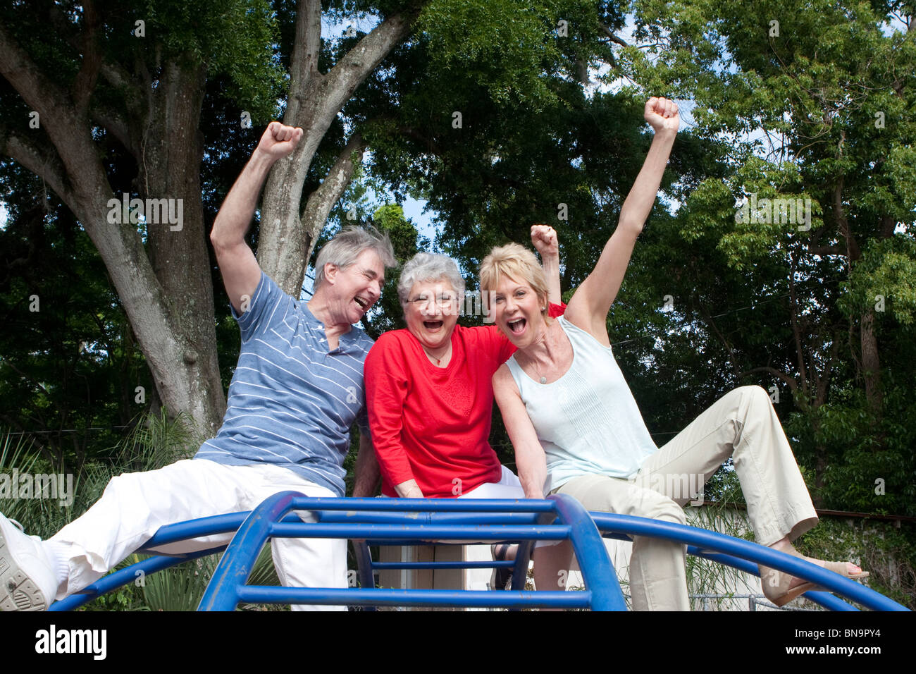 Three seniors sitting on top of playground equipment celebrating Stock