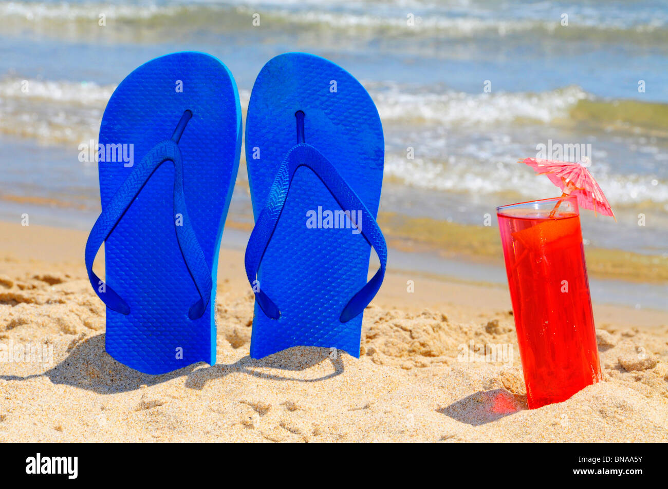 a pair of flip-flops and a cocktail on the beach Stock Photo