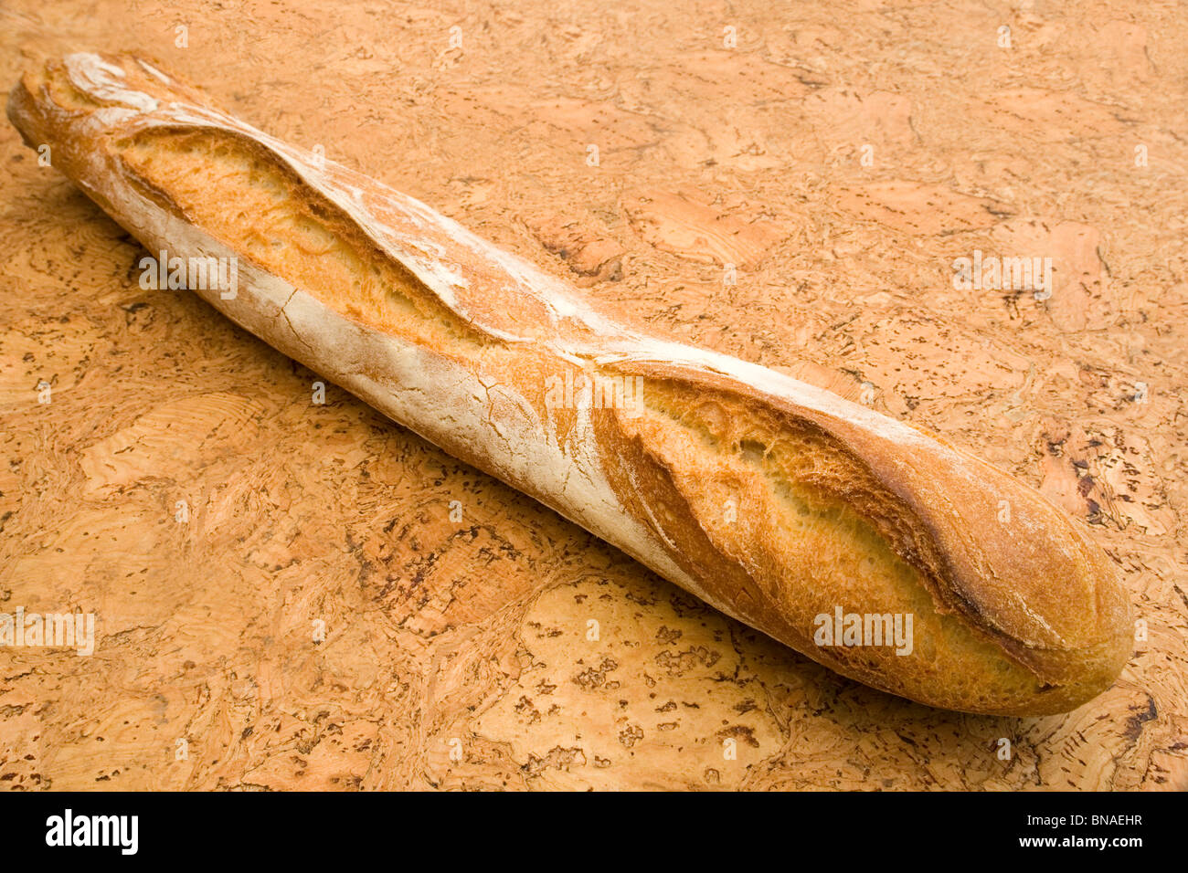 A traditional French stick of bread on a cork background (France). Baguette traditionnelle de pain sur fond de liège (France). Stock Photo