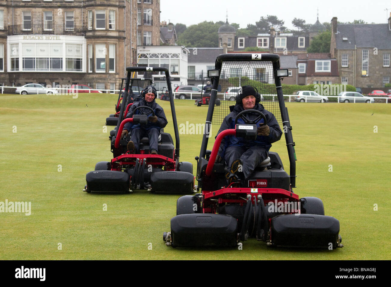 Riding Greens mowers machinery Grass cutters and Green keepers mowing the Old Course;  Team maintenance at the 139th British Open Golf 2010, July 15-18, St Andrews, Scotland, UK. The  function of mowing is to prepare the golf course for play although mowing patterns are often used to highlight  features of a golf course. The mowing pattern can have a big impact on the appearance of the golf course and the health of the turf while affecting your labor and fuel consumption line items. The most common fairway mowing methods are striping, contour mowing, the classic cut, and pushing and pulling. Stock Photo