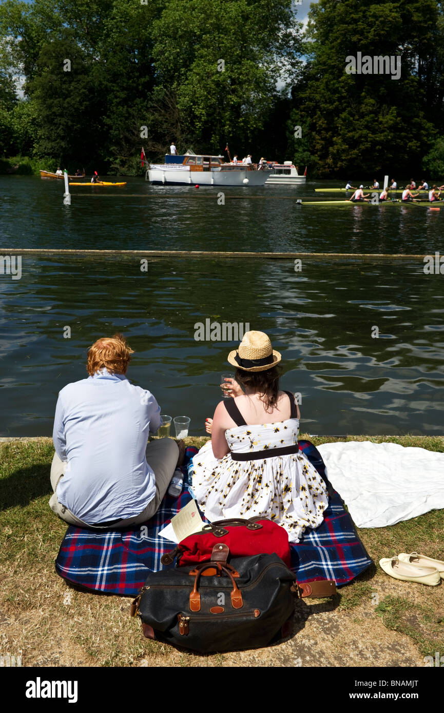 A couple, a man and woman sitting on a picnic rug on the riverbank of the River Thames enjoying Henley Royal Regatta. Stock Photo