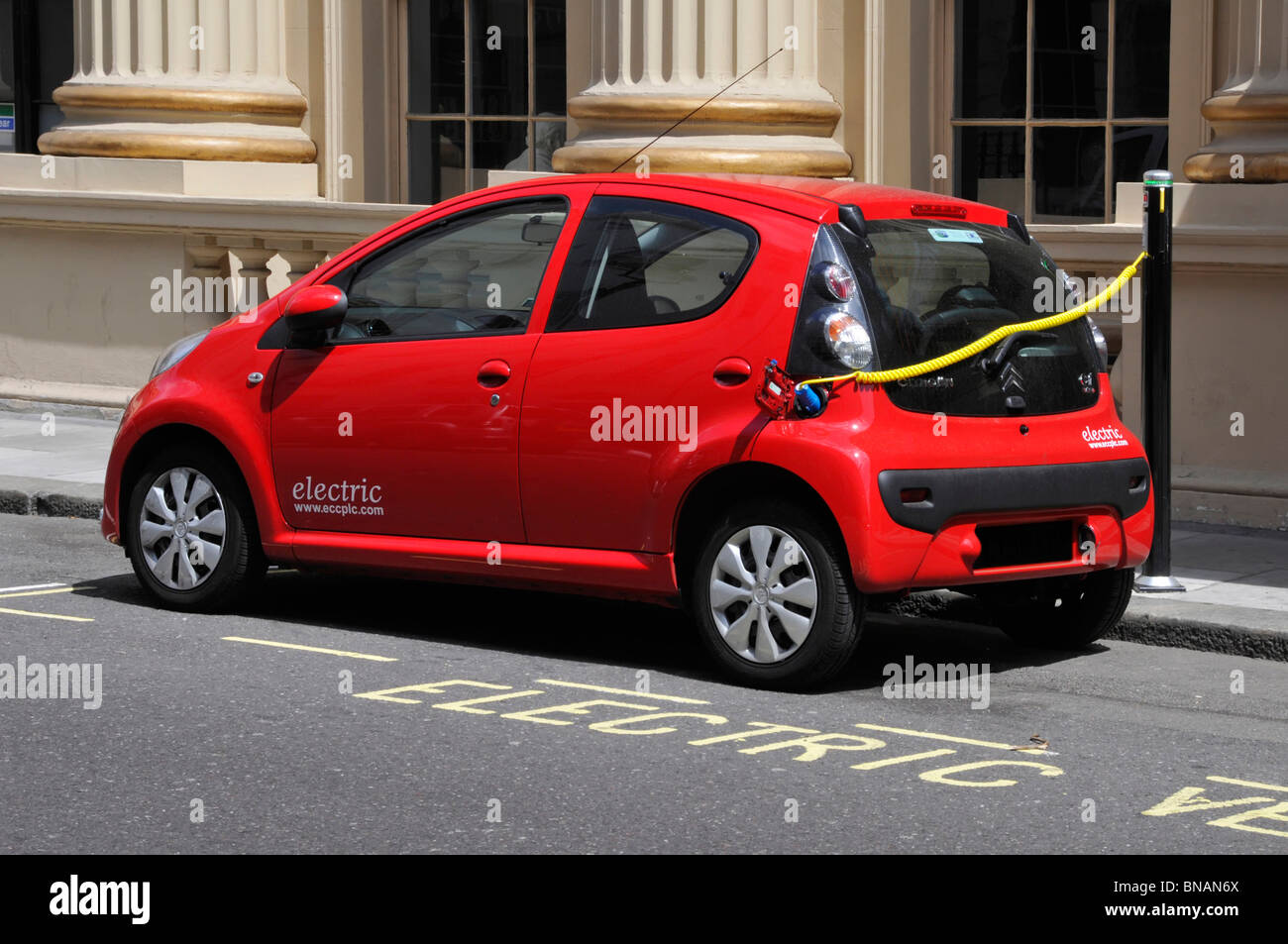 Electric car charging via public charging station on pavement mounted bollard beside marked out designated parking bay Westminster London  England UK Stock Photo