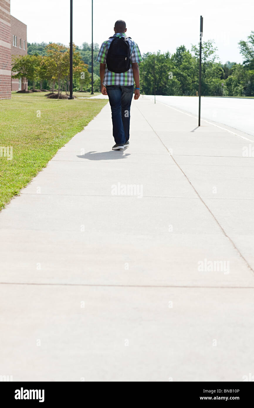 Male high school student walking along pavement Stock Photo