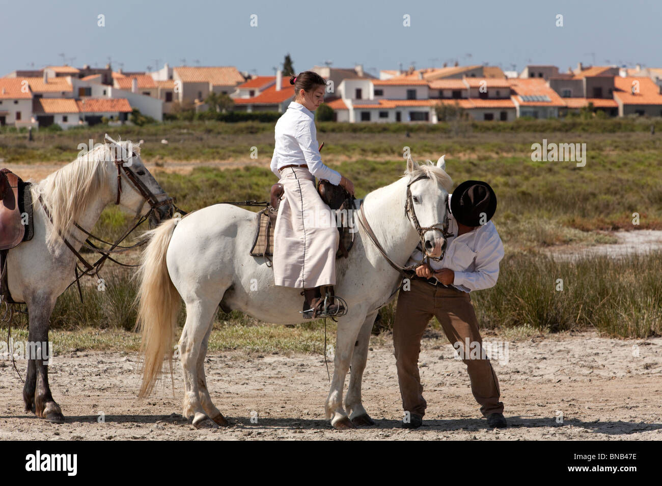 young female gardian, cowgirl of the Camargue region, on her horse, cowboy helping with the horses bridle Stock Photo