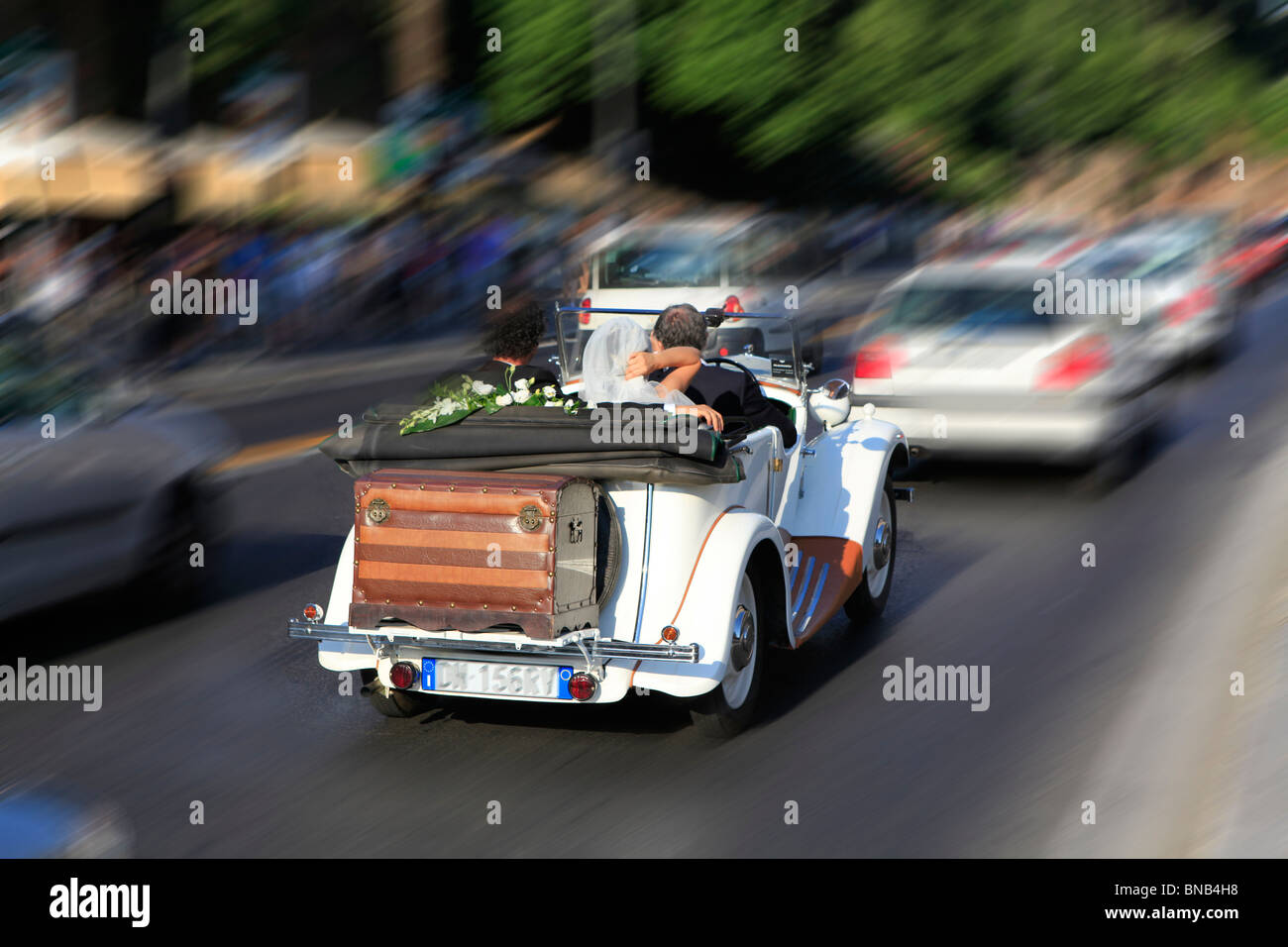Newly wed couple speed through city in open top sports car Stock Photo
