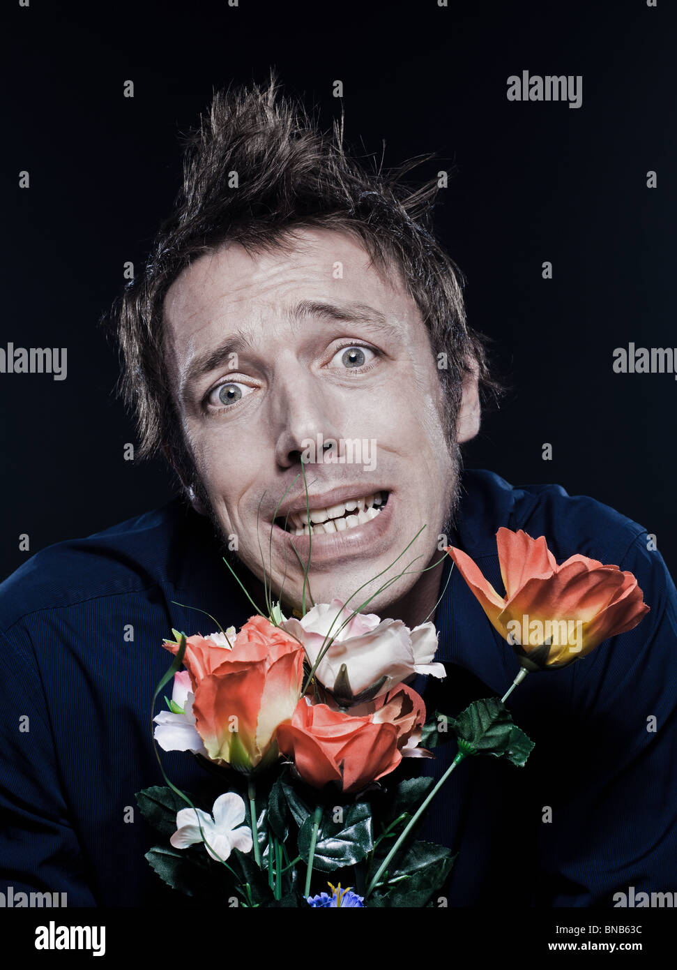 studio portrait on black background of a funny expressive caucasian man offering flowers stressed Stock Photo