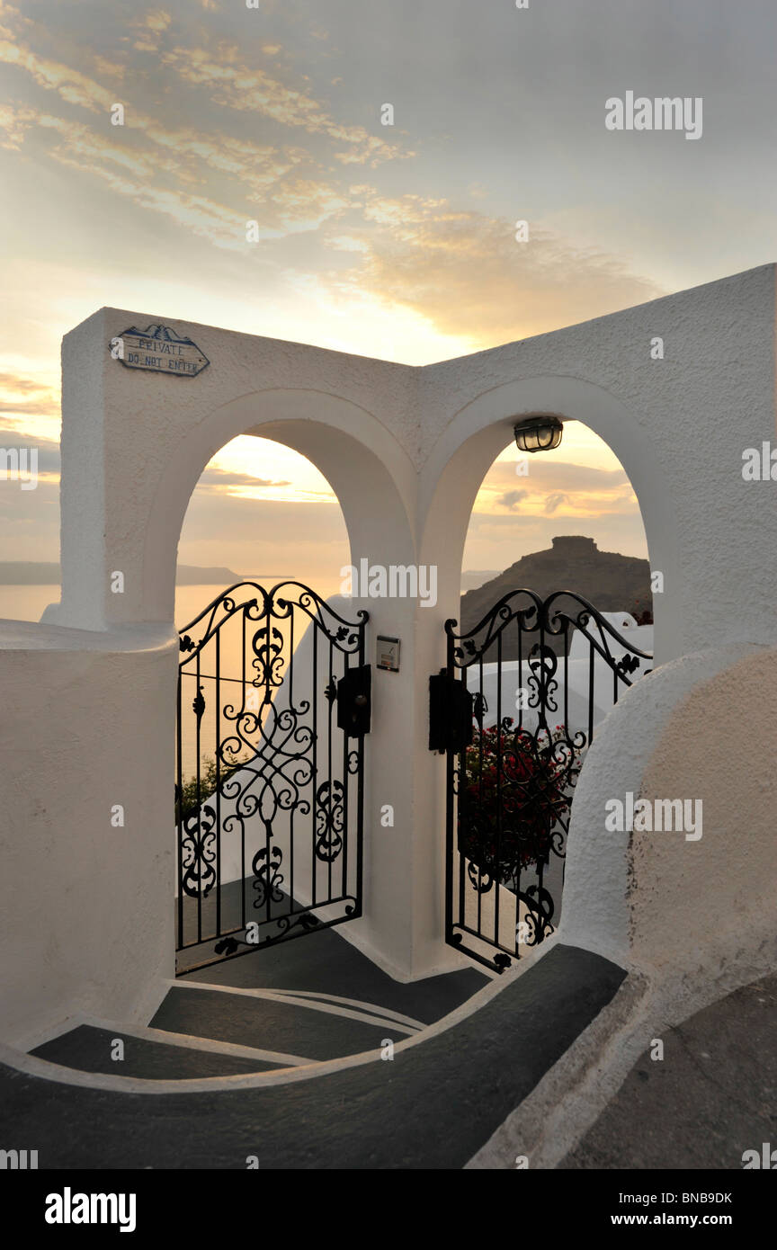 Wrought iron gates leading to 2 houses on the Greek Island of Santorini Cyclades Greece with the sun setting over the horizon Stock Photo