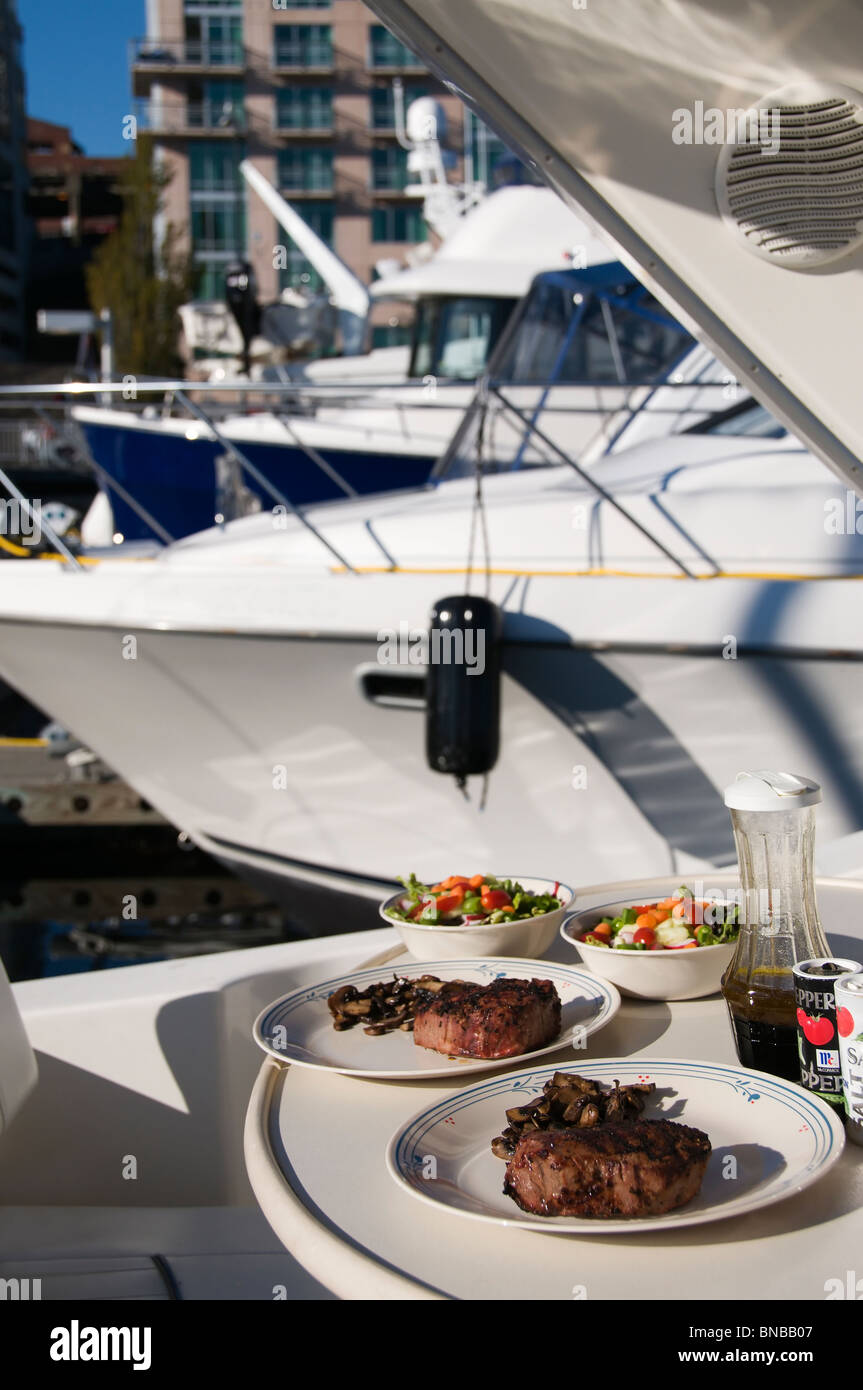 Steaks and salads are served on a boat's outdoor dining table in Bell Harbor Marina in Seattle, Washington. Stock Photo