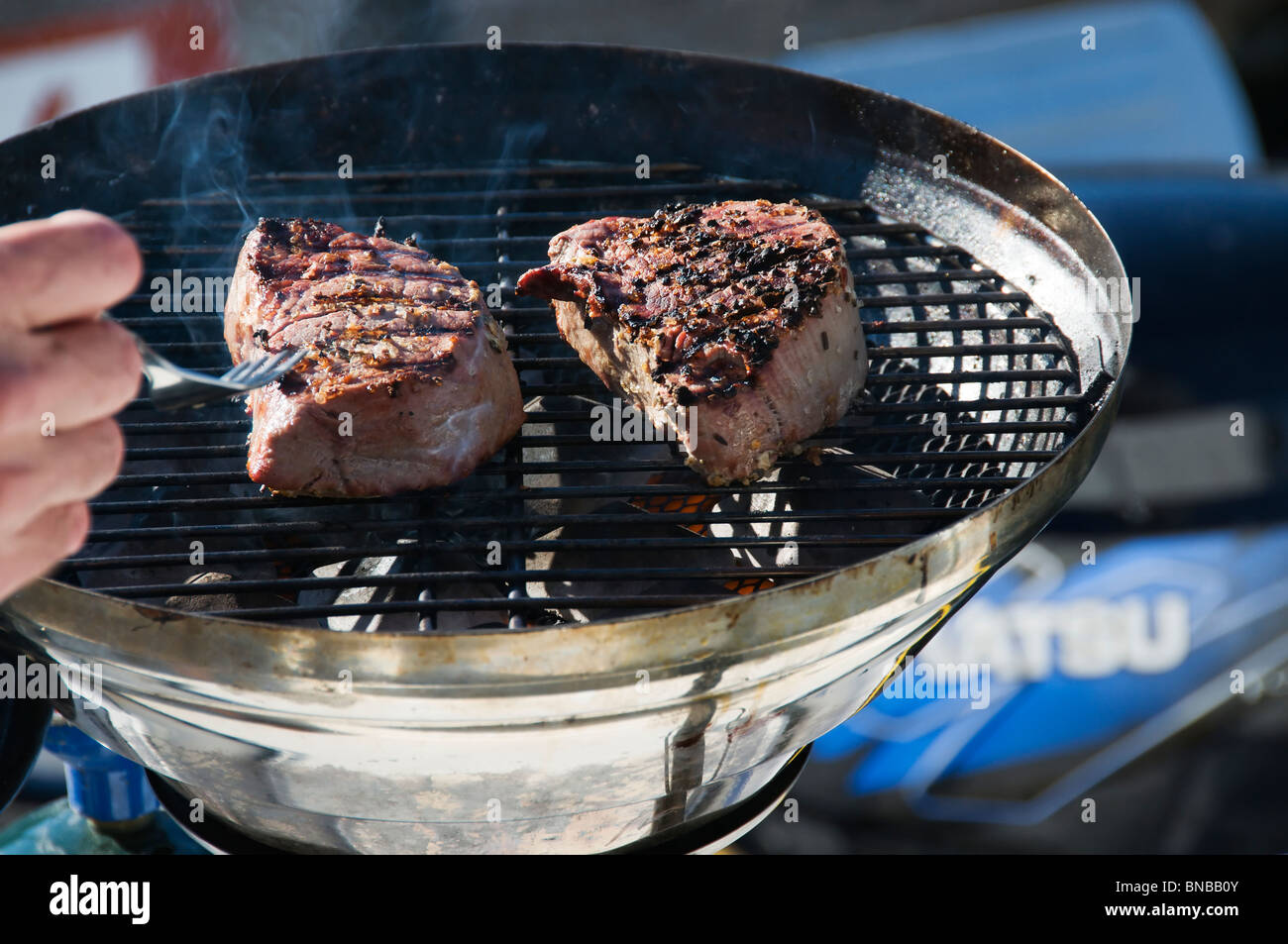 Two filet mignon steaks are being grilled on a round outdoor barbecue on the back of a boat. Stock Photo