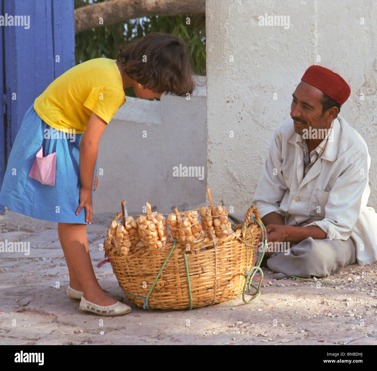 Tunisia, Sidi Bou Said. Girl Buying Cookies, Biscuits, from Man Wearing a Chechia, a Traditional Tunisian Hat. Stock Photo
