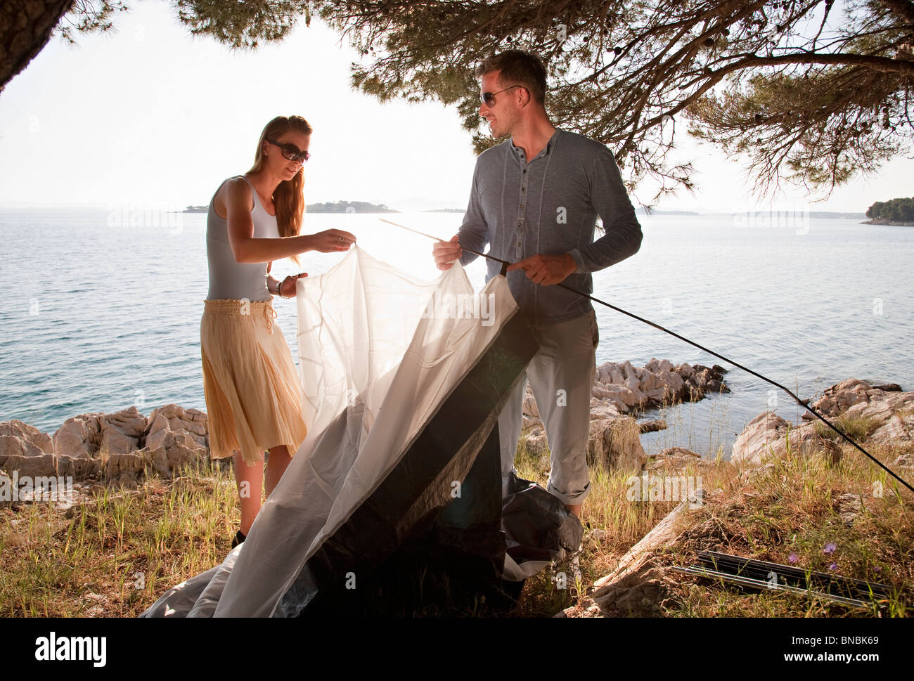 Couple putting up tent by sea Stock Photo