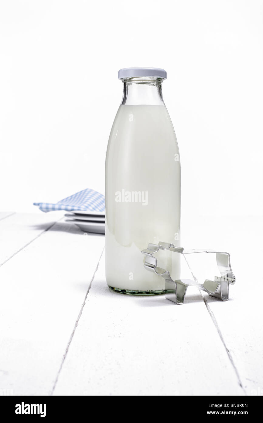 Milchflasche und kuhfoermige Ausstechform auf weissen Holztisch Stock Photo