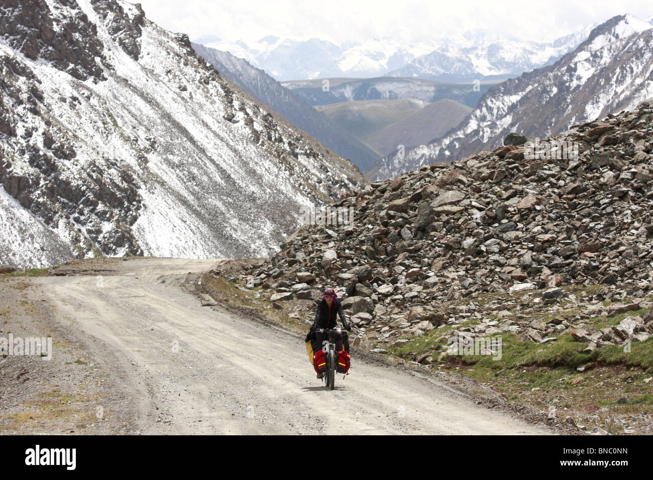Female cyclist on a mountain road to Chongashuu Pass (3820 metres above the sea level), Kyrgyzstan Stock Photo