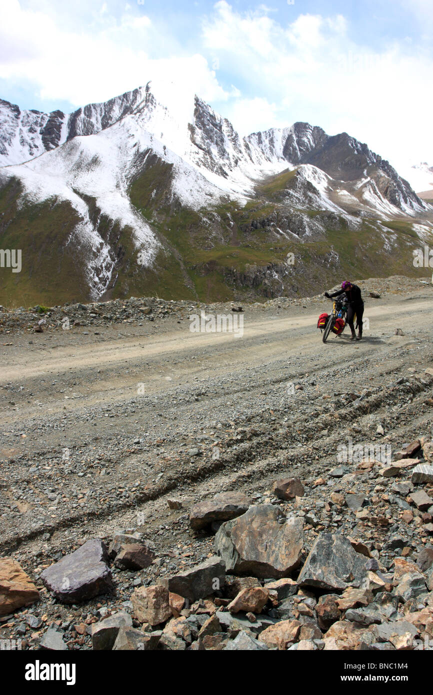 Female cyclist on a mountain road to Chongashuu Pass (3820 metres above the sea level), Kyrgyzstan Stock Photo