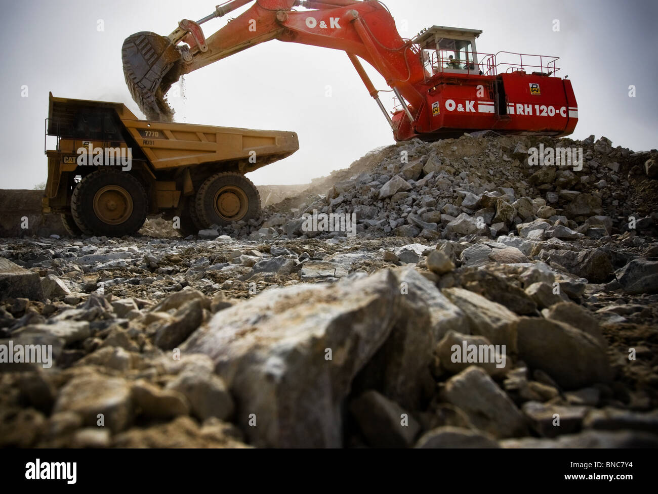 An excavator loads a large truck with ore in the main pit of the Youga gold mine near the town of Youga Stock Photo