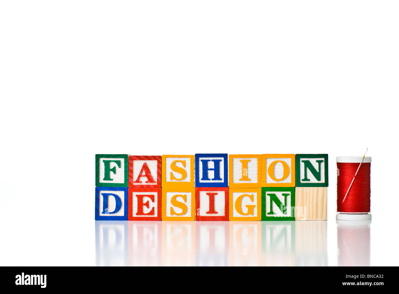 Colorful children's blocks spelling FASHION DESIGN with a spool of thread and needle Stock Photo