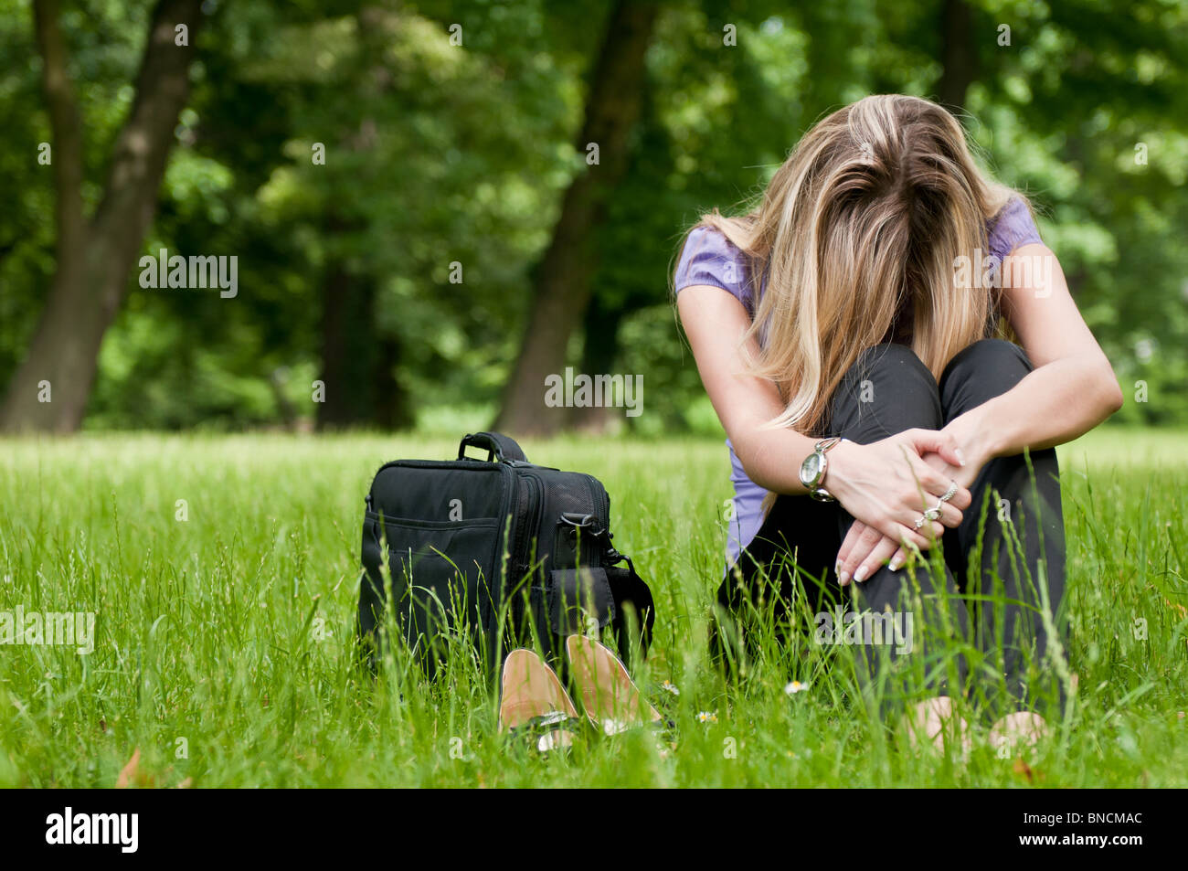 Young depressed business woman siting in grass - notebook bag and shoes lying next Stock Photo