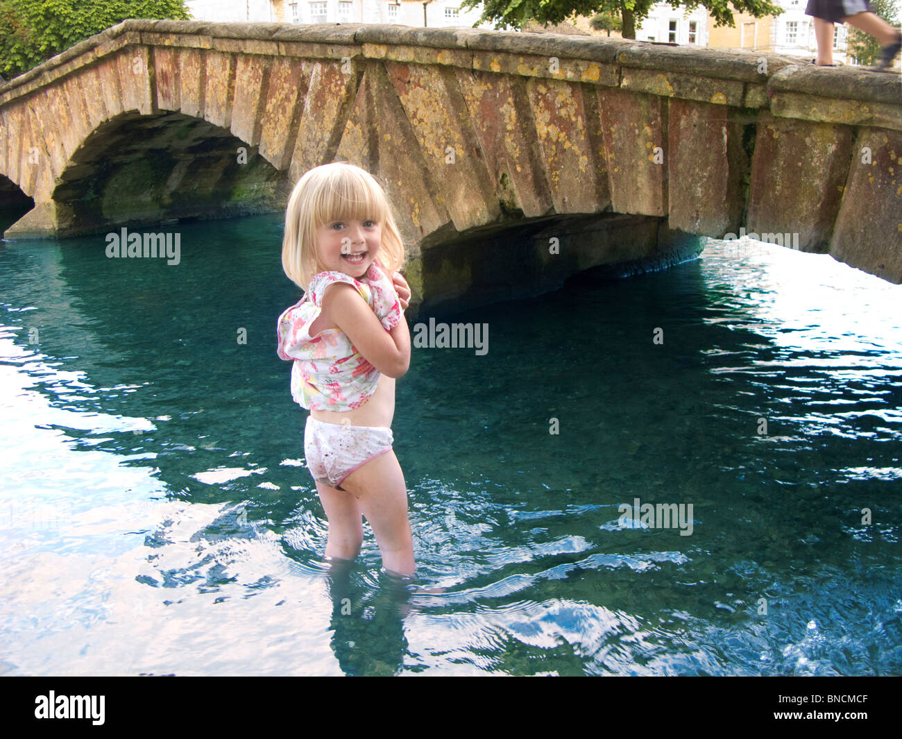 A little girl paddling in a stream. Bourton on the Water, The Cotswolds, England. Stock Photo