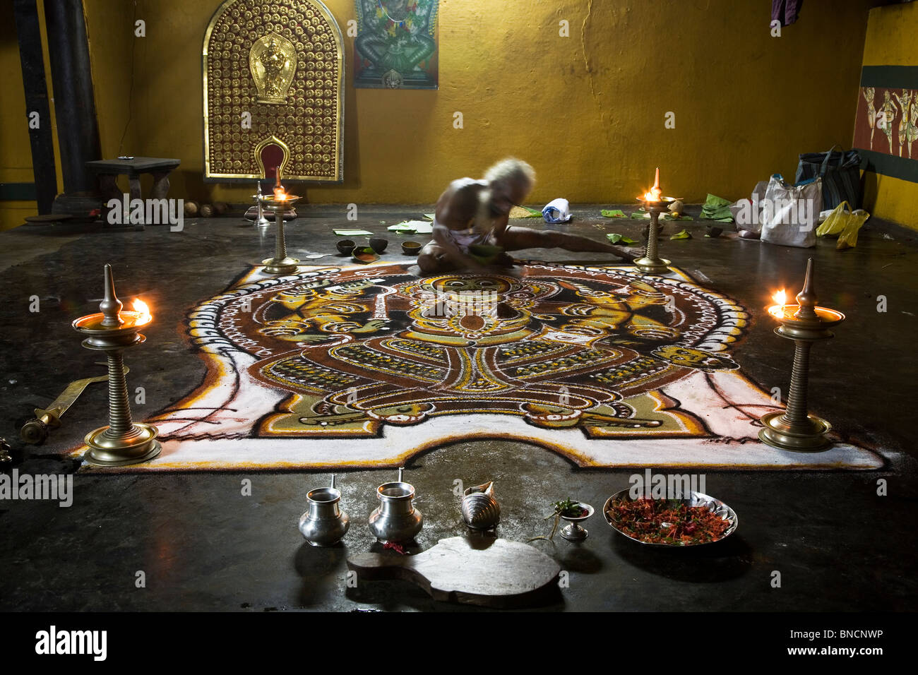 A Namboodiri Brahmin priest completes a Kalam floor image of the Hindu goddess Kali at a temple in Kerala, India. Stock Photo