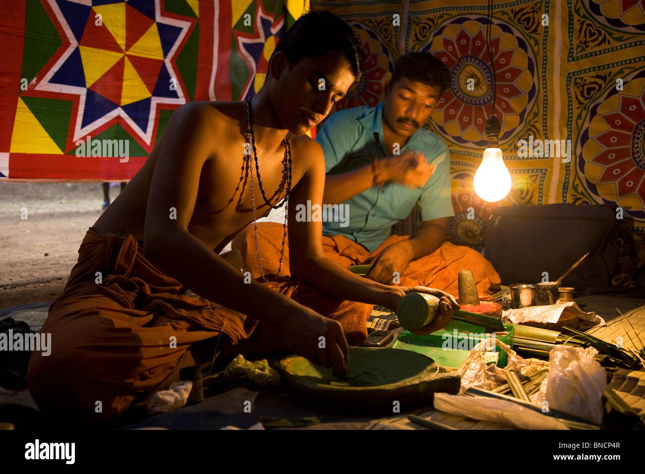 Kathakali actors prepare make up by blending minerals and coconut oil before a performance. Stock Photo