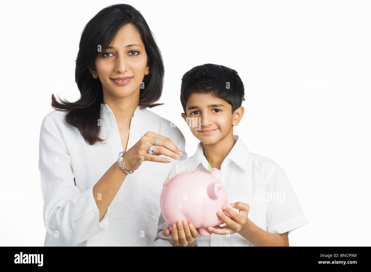 Woman holding a coin over a piggy bank held by her son Stock Photo - Alamy