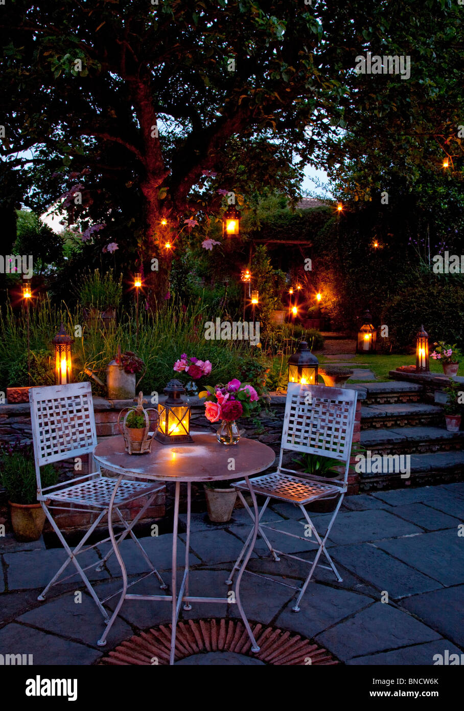 Metal table and chairs on patio with candles and lanterns in garden at night Stock Photo