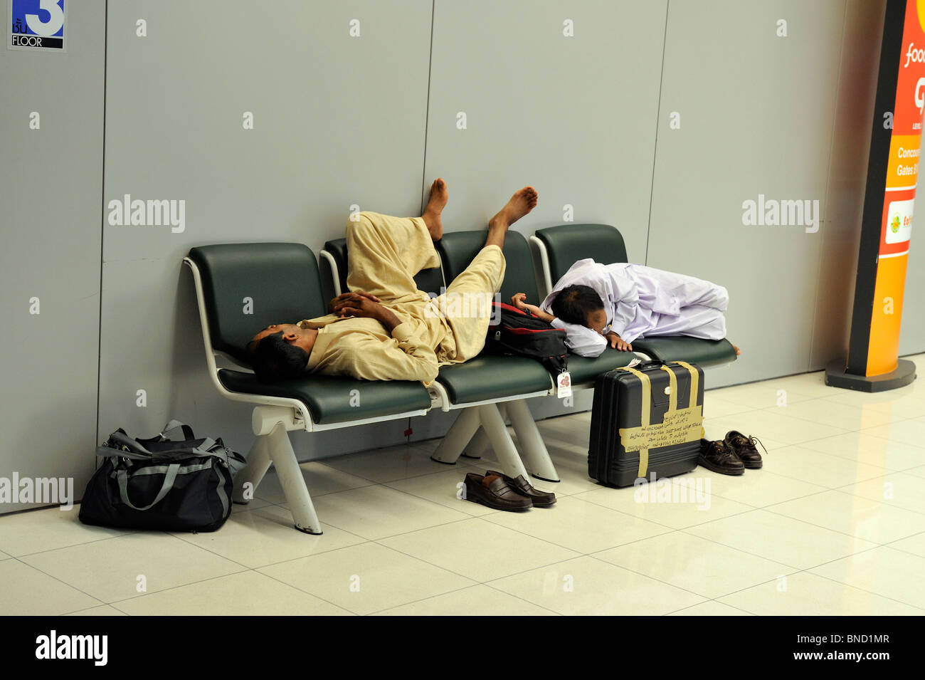 Two passengers sleeping on benches in Suvarnabhumi Airport. Bangkok