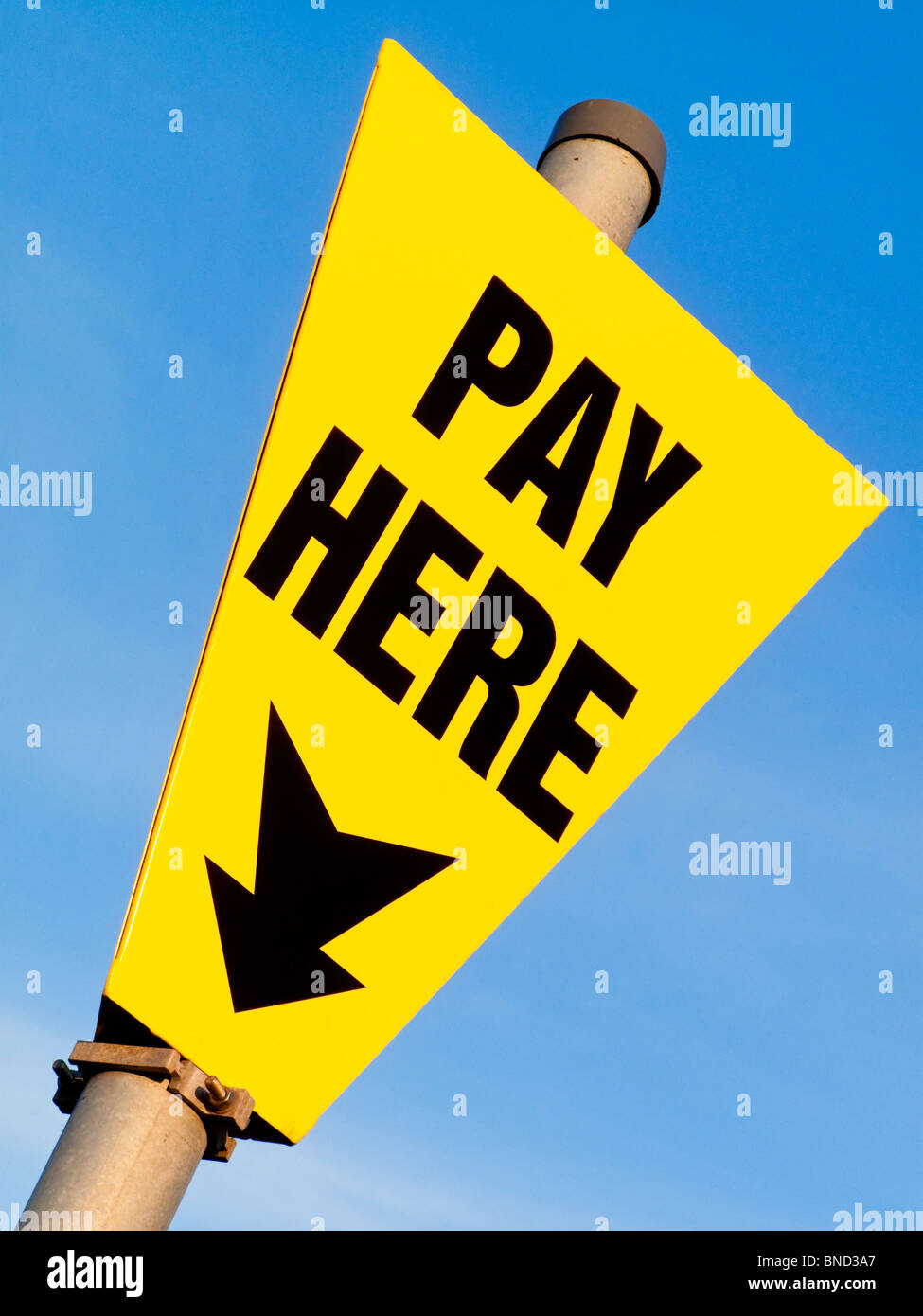 Yelow Pay Here sign in car park with blue sky behind and black text with arrow pointing down Stock Photo