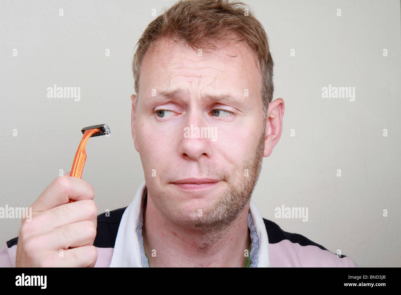 Half shaved and confused white male looks at a razor deciding whether to shave the rest of his beard off Stock Photo