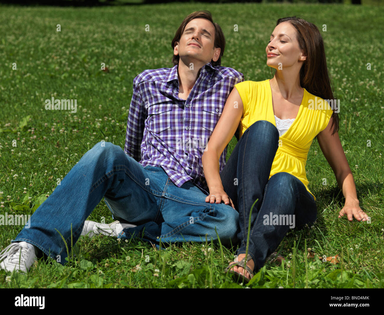 Young happy couple in their early thirties sitting on grass in a park ...