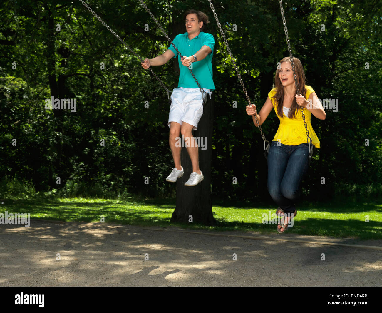 Young couple in their thirties having fun on a swing at children's playground Stock Photo