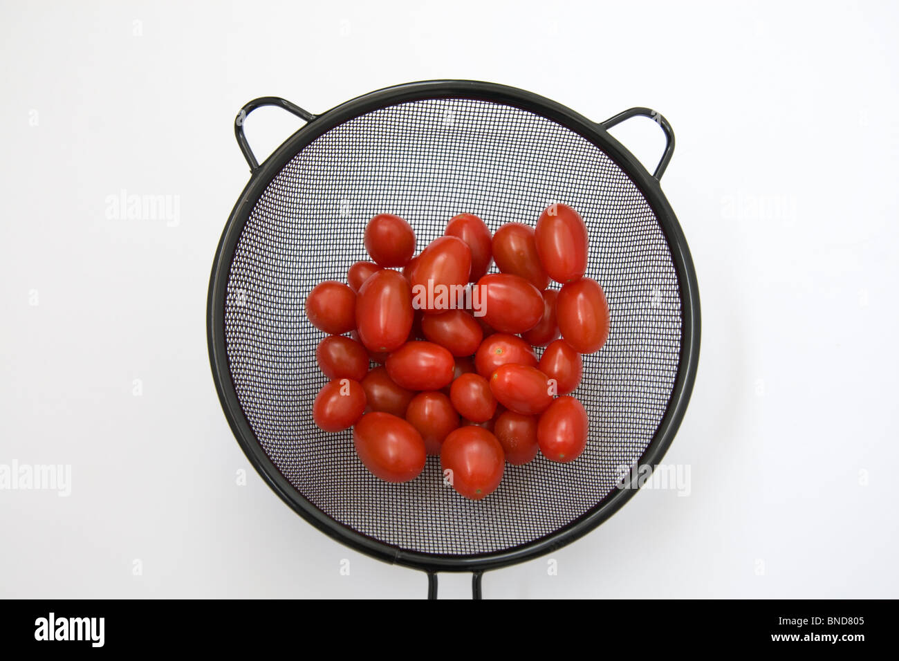 plum tomatoes in a black sieve against a white ground Stock Photo