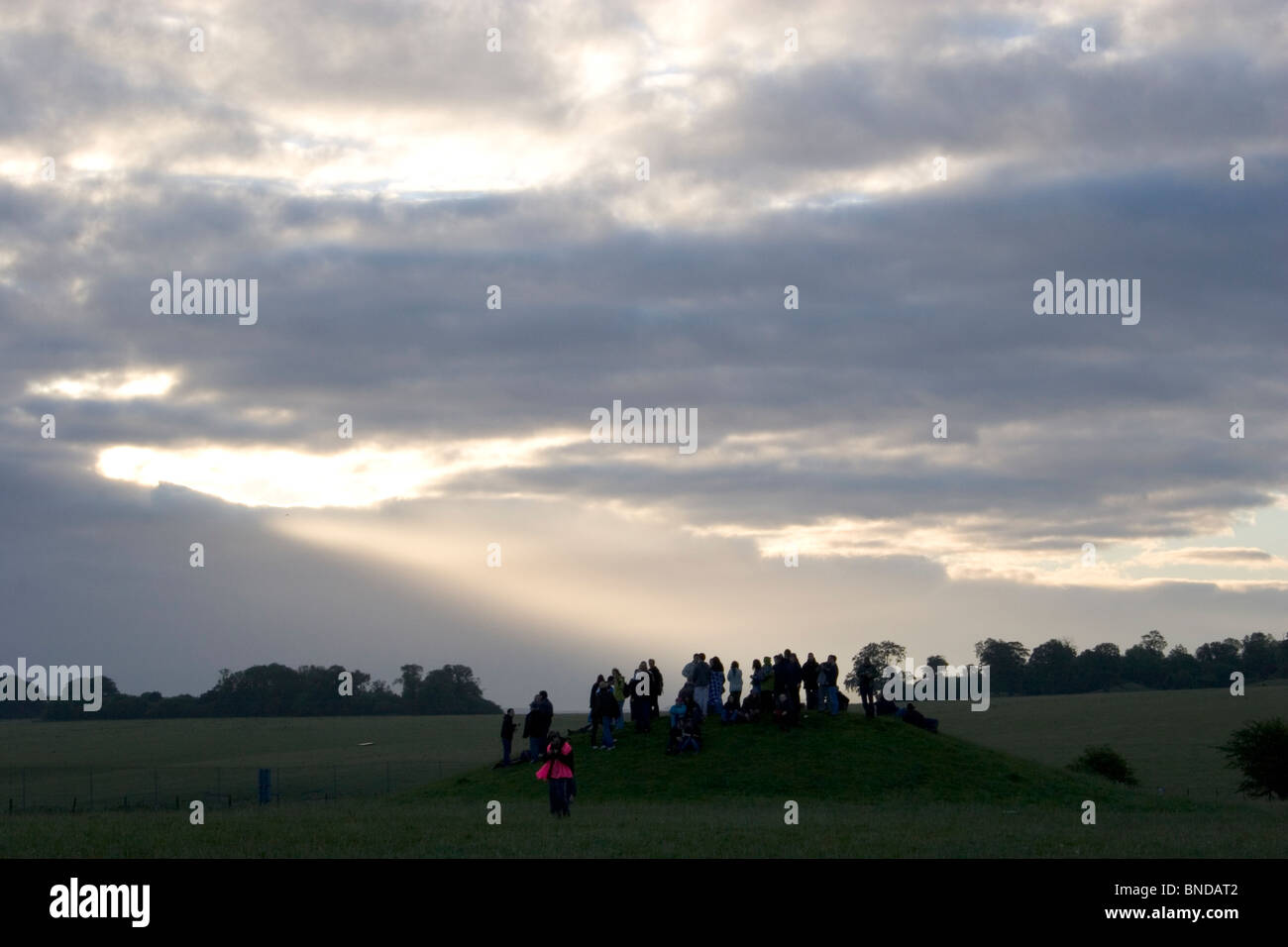 People standing on Bronze age burial mound watching sunrise during summer solstice at Stonehenge, Wiltshire, UK Stock Photo