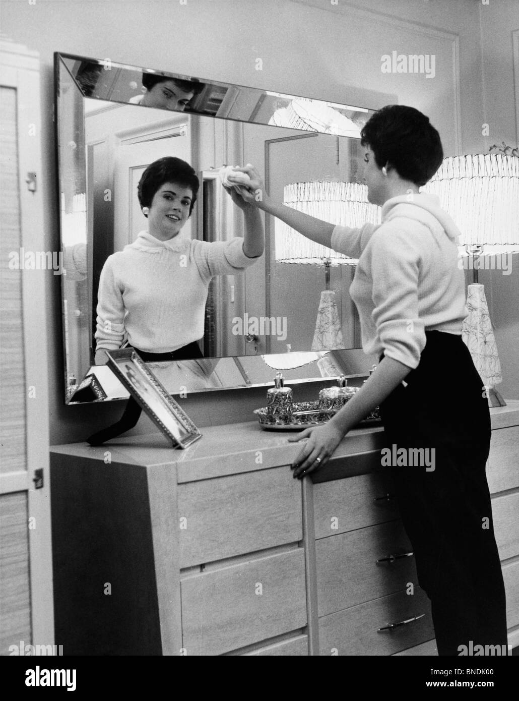 Side profile of a young woman cleaning the mirror of a dressing table
