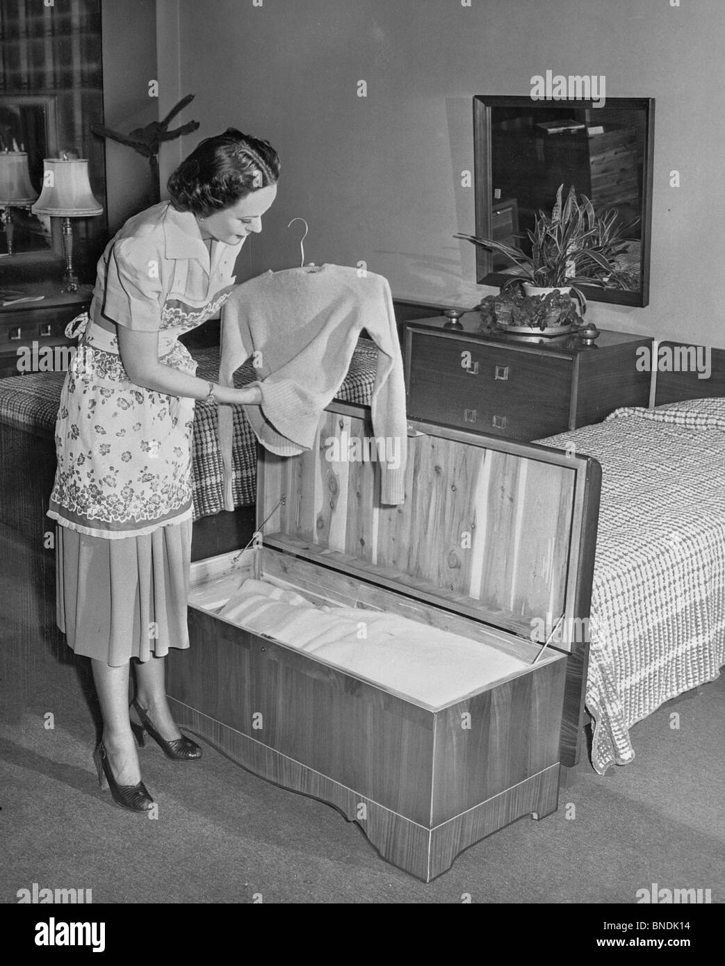 Side profile of a young woman putting clothes in a cedar chest Stock