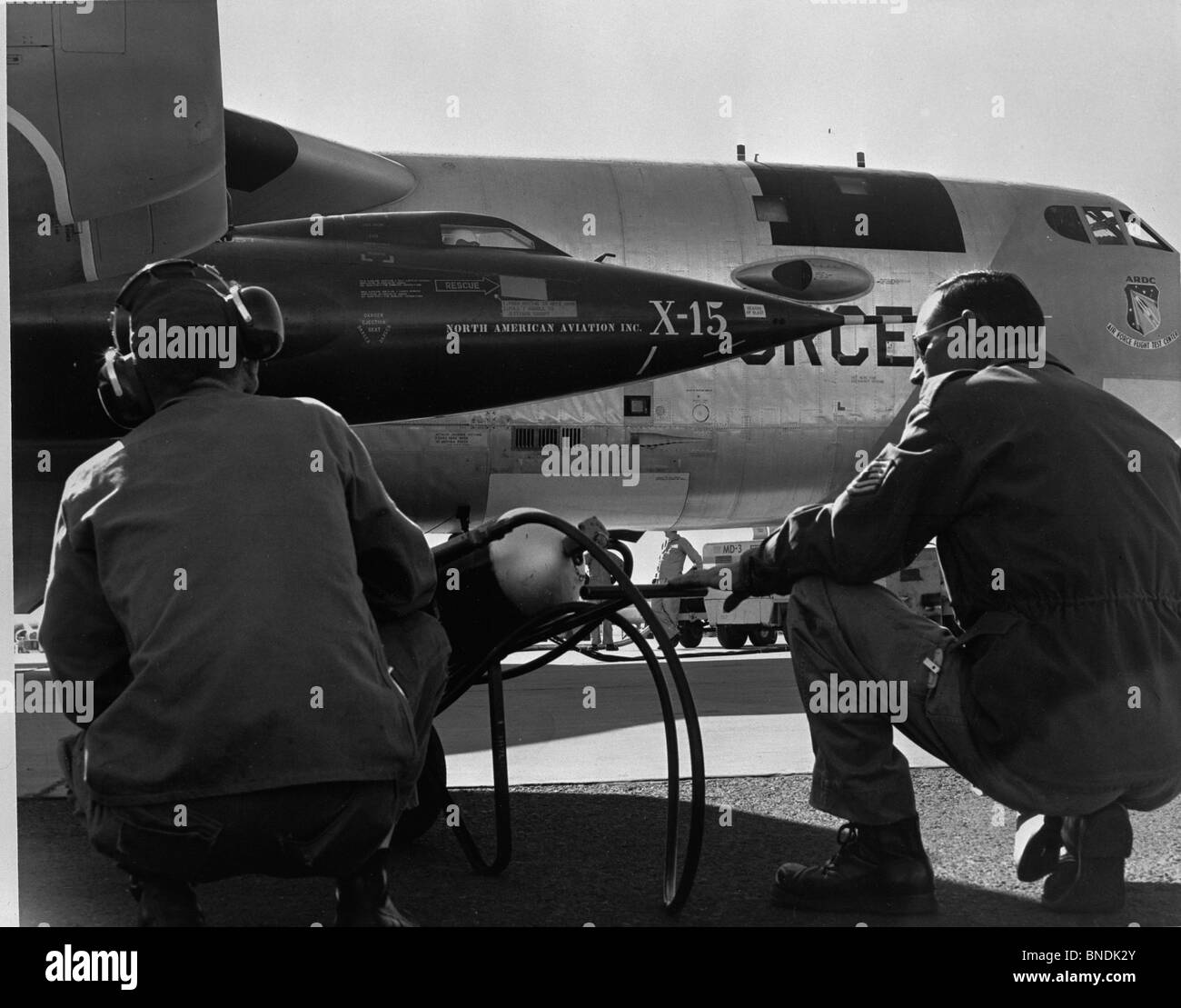 Rear view of two men crouching near fighter planes, X-15 Rocket Research Airplane, B-52 Mothership Stock Photo