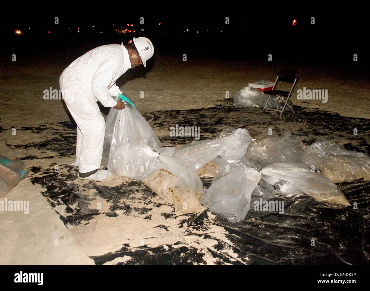 A night crew worker wearing a Tyvek suit, bags up large quantities of oil from the British Petroleum oil spill on a beach in MS. Stock Photo