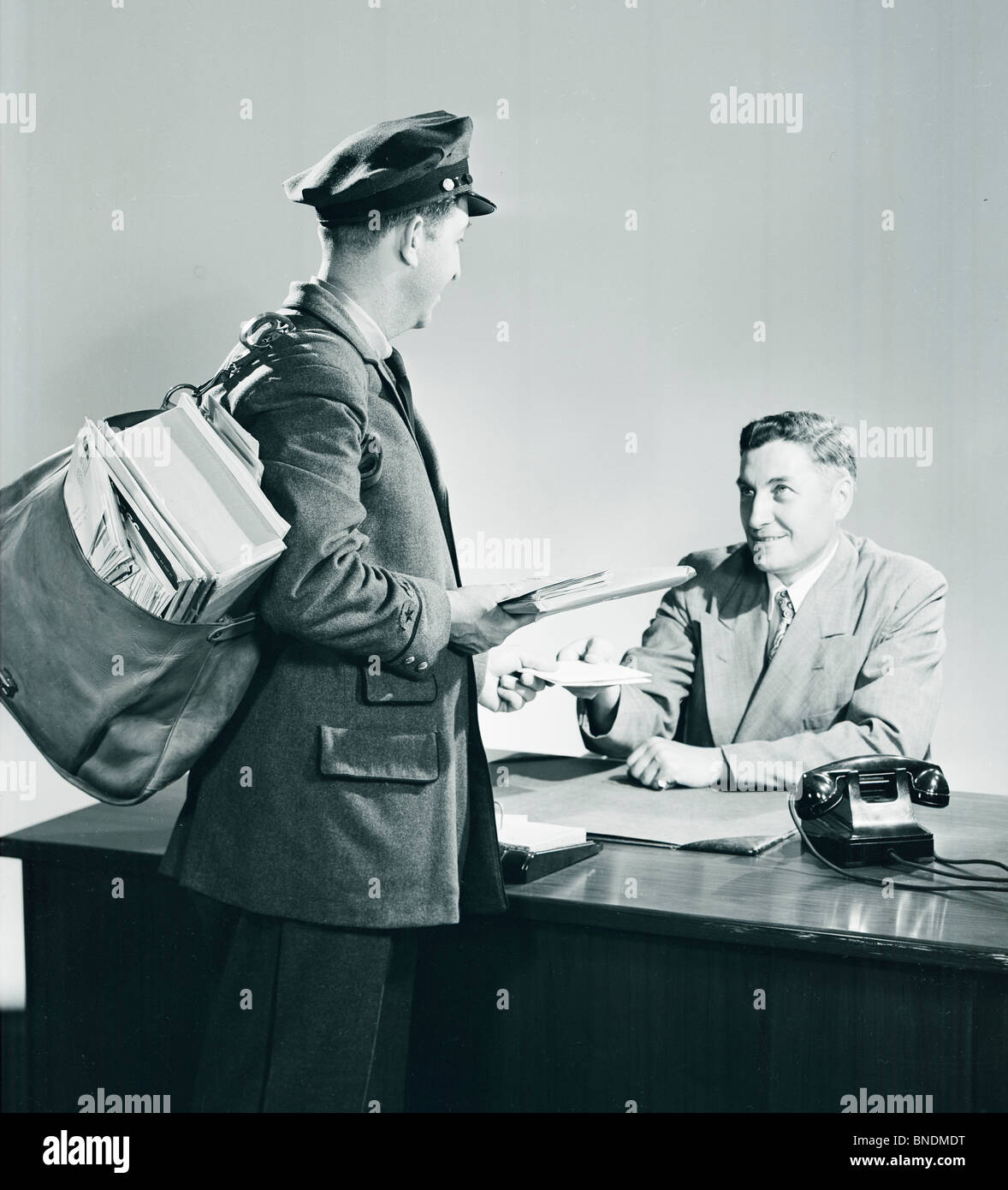 Postman bringing mail to a man sitting behind desk Stock Photo
