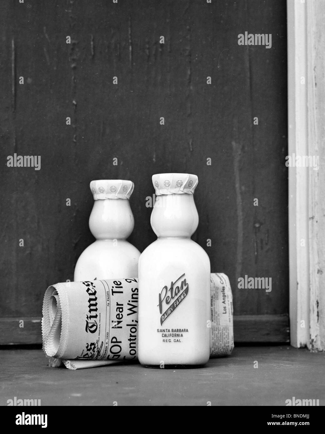 Two milk bottles with a newspaper at a doorstep Stock Photo Alamy