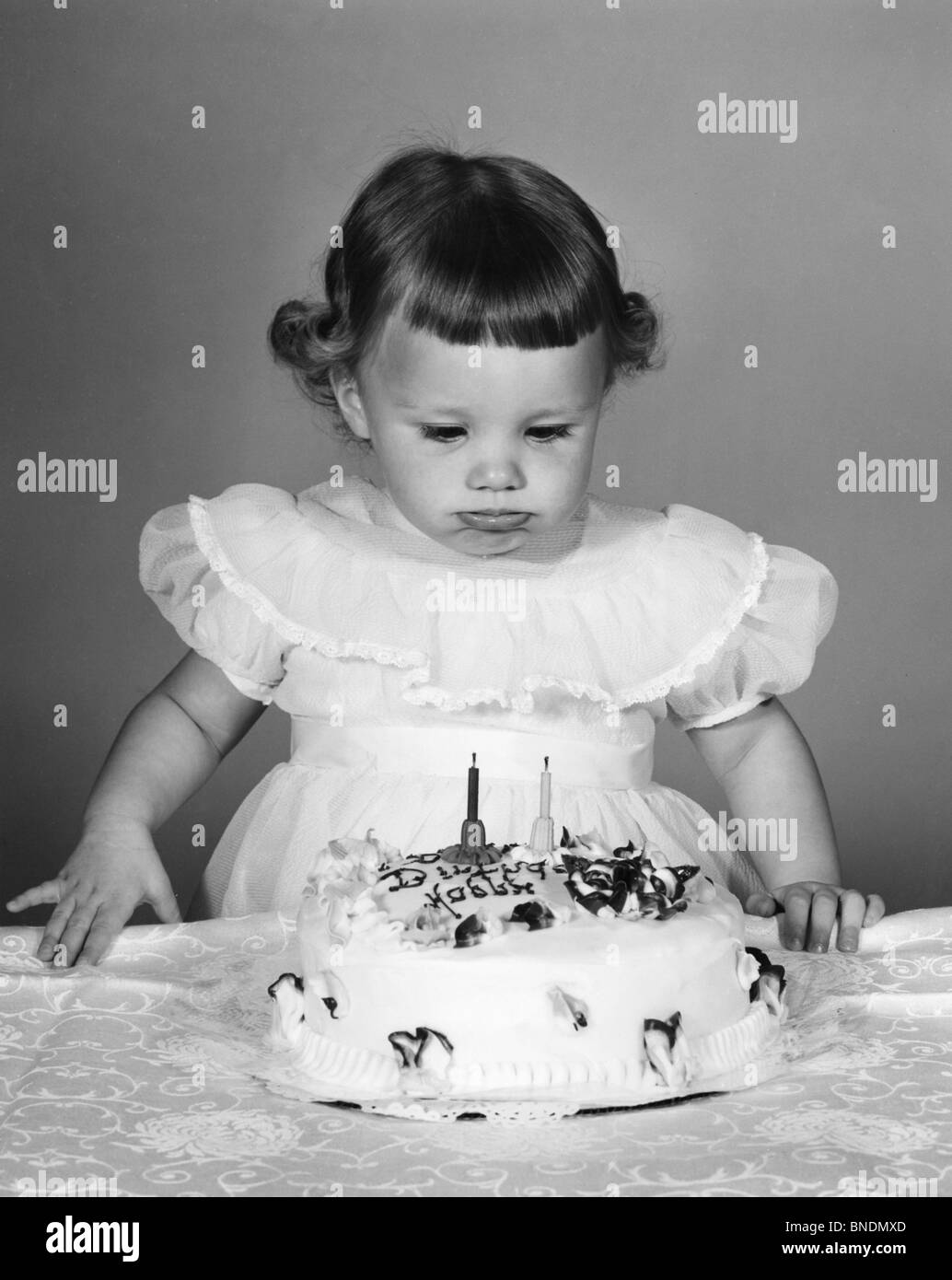 Girl looking at birthday cake, making a face Stock Photo