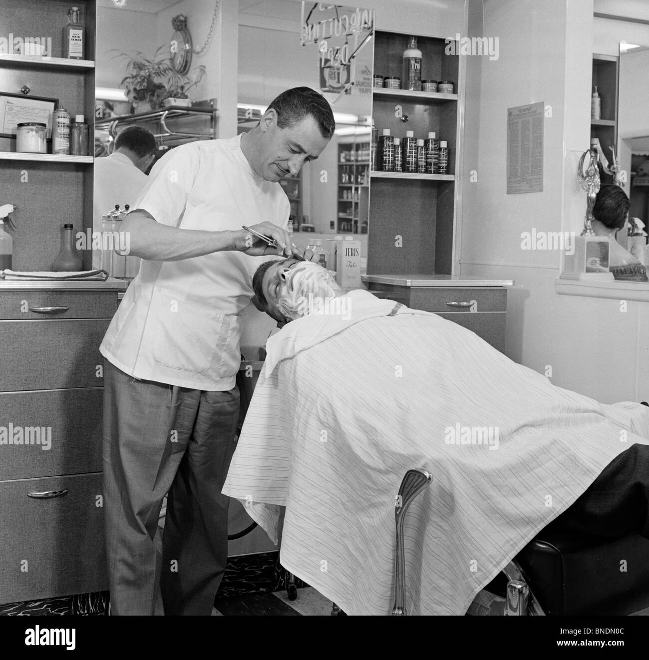 Barber shaving a mid adult man in a hair salon Stock Photo
