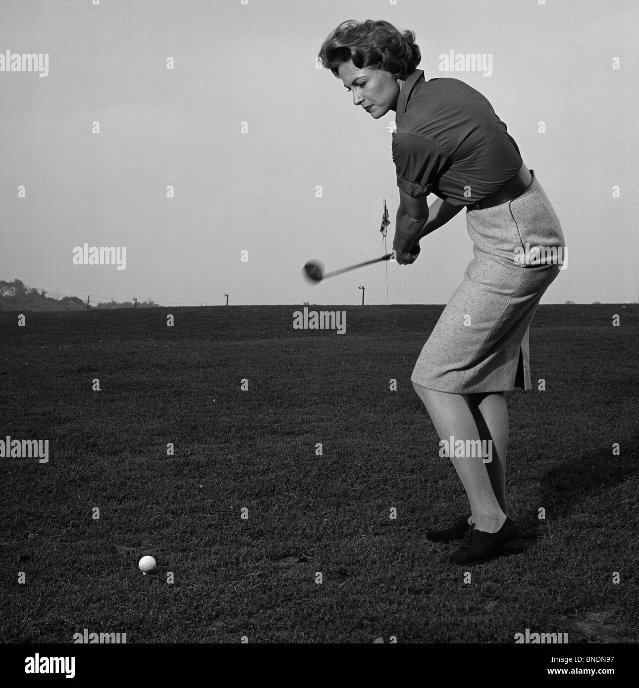 Mid adult woman swinging a golf club on a golf course Stock Photo