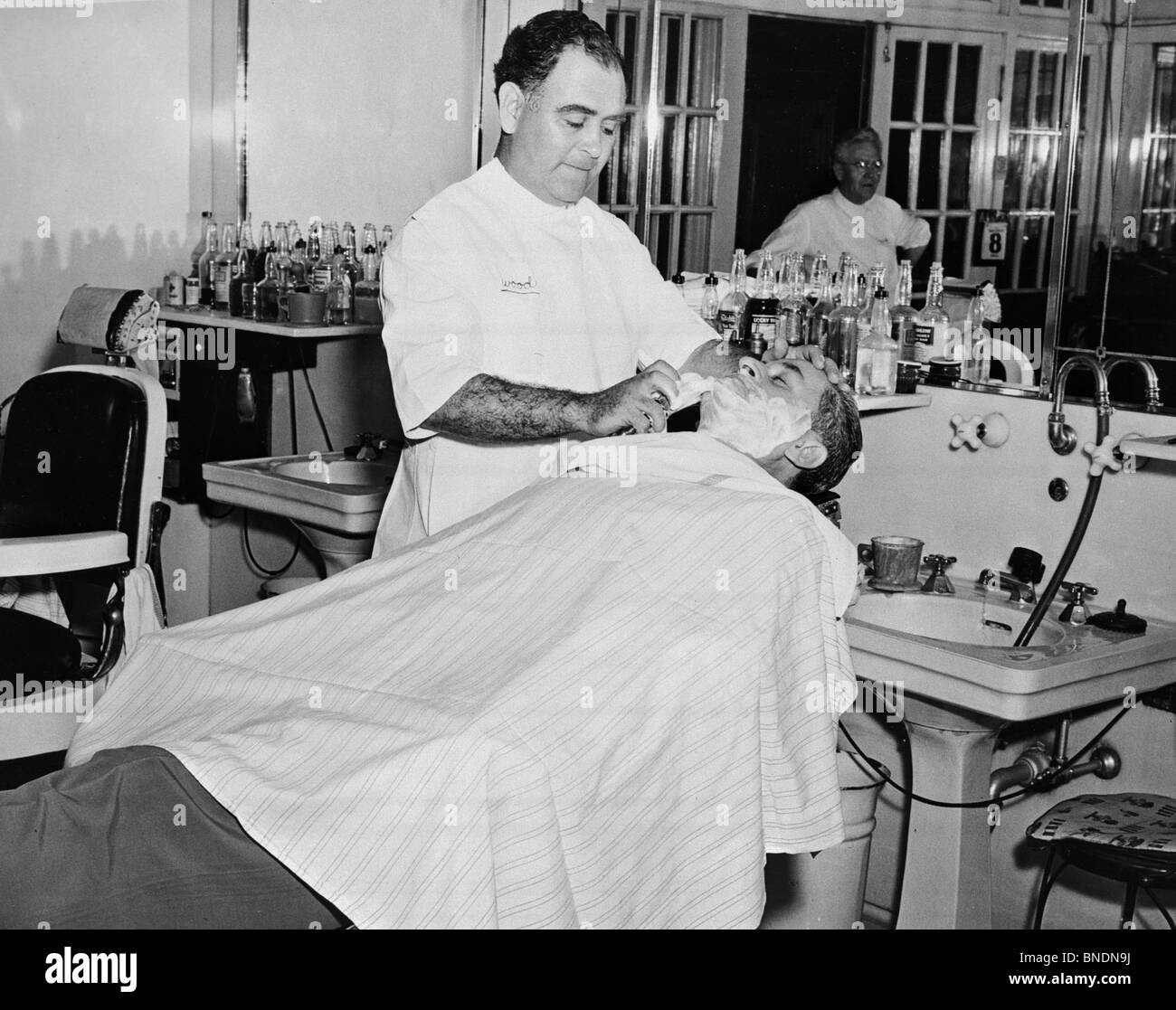 Barber shaving a mid adult man in a barbershop Stock Photo