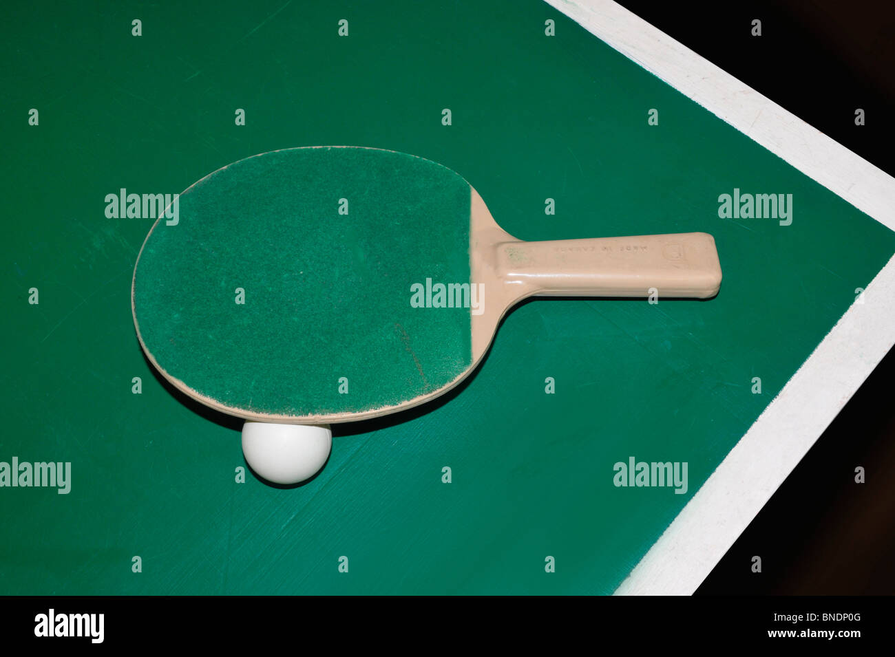 A table tennis bat and ball sit on the edge of a table tennis table. Stock Photo