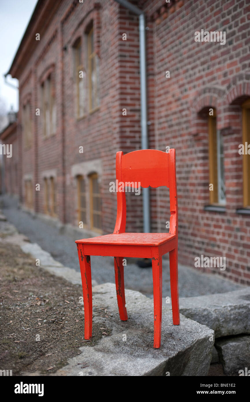 Bright orange antique wooden chair standing in front of an old brick building Stock Photo