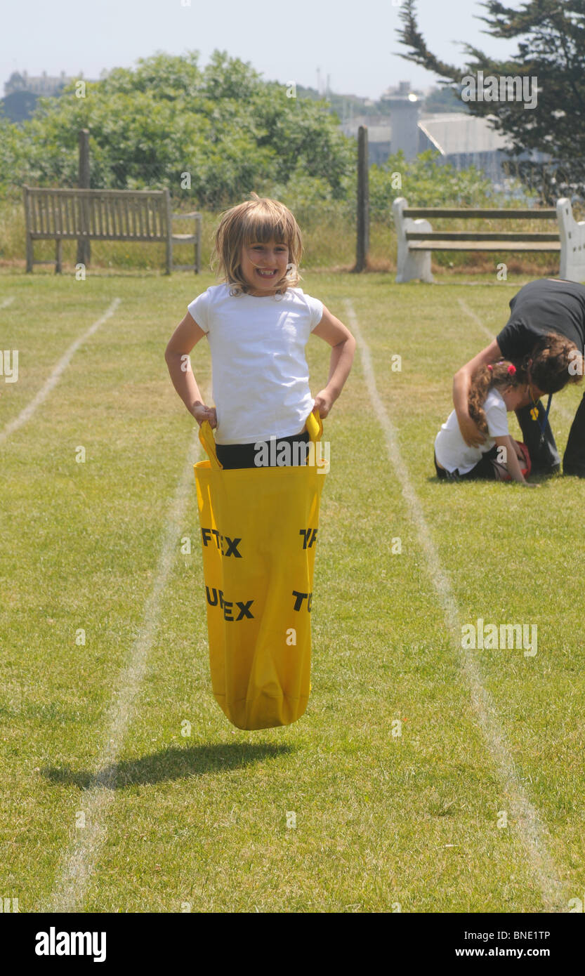 A 7 year old girl in the school sack race whilst a fallen child is comforted in the background Stock Photo