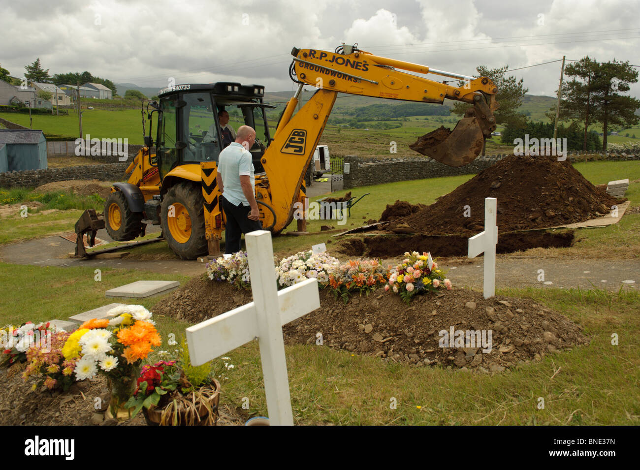 Contractor digging grave with a JCB digger in Steshon village near Trawsfynydd, Snowdonia National Park, Gwynedd North Wales UK Stock Photo