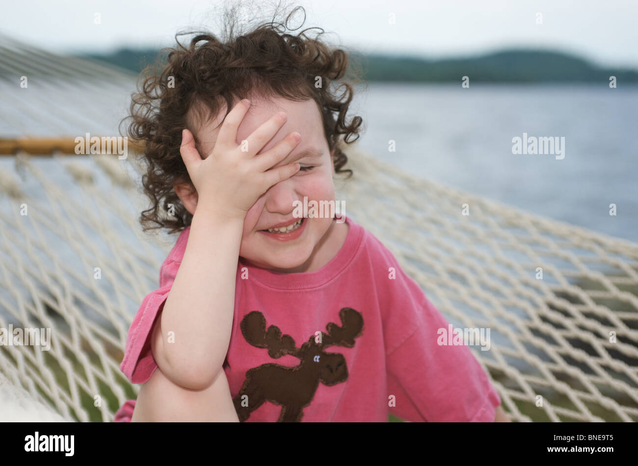 cute little girl sitting on a hammock, laughing and slapping her hand to her forehead Stock Photo