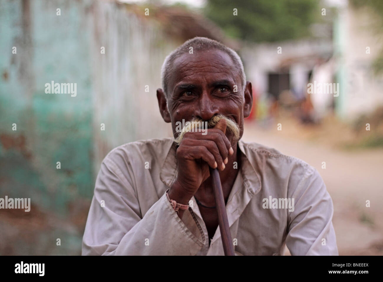 An Old Indian man sitting on a cot outside his house and smoking a hookah in a remote village in India Stock Photo